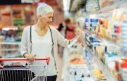 A woman is grocery shopping and reading food labels